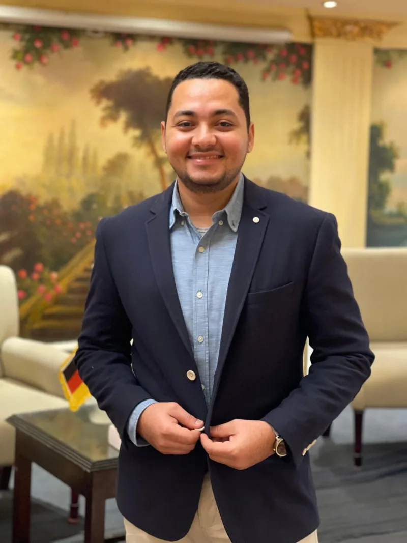 أحمد عصام، مؤسس Piece of German، مبتسمًا ويرتدي سترة كحلية
